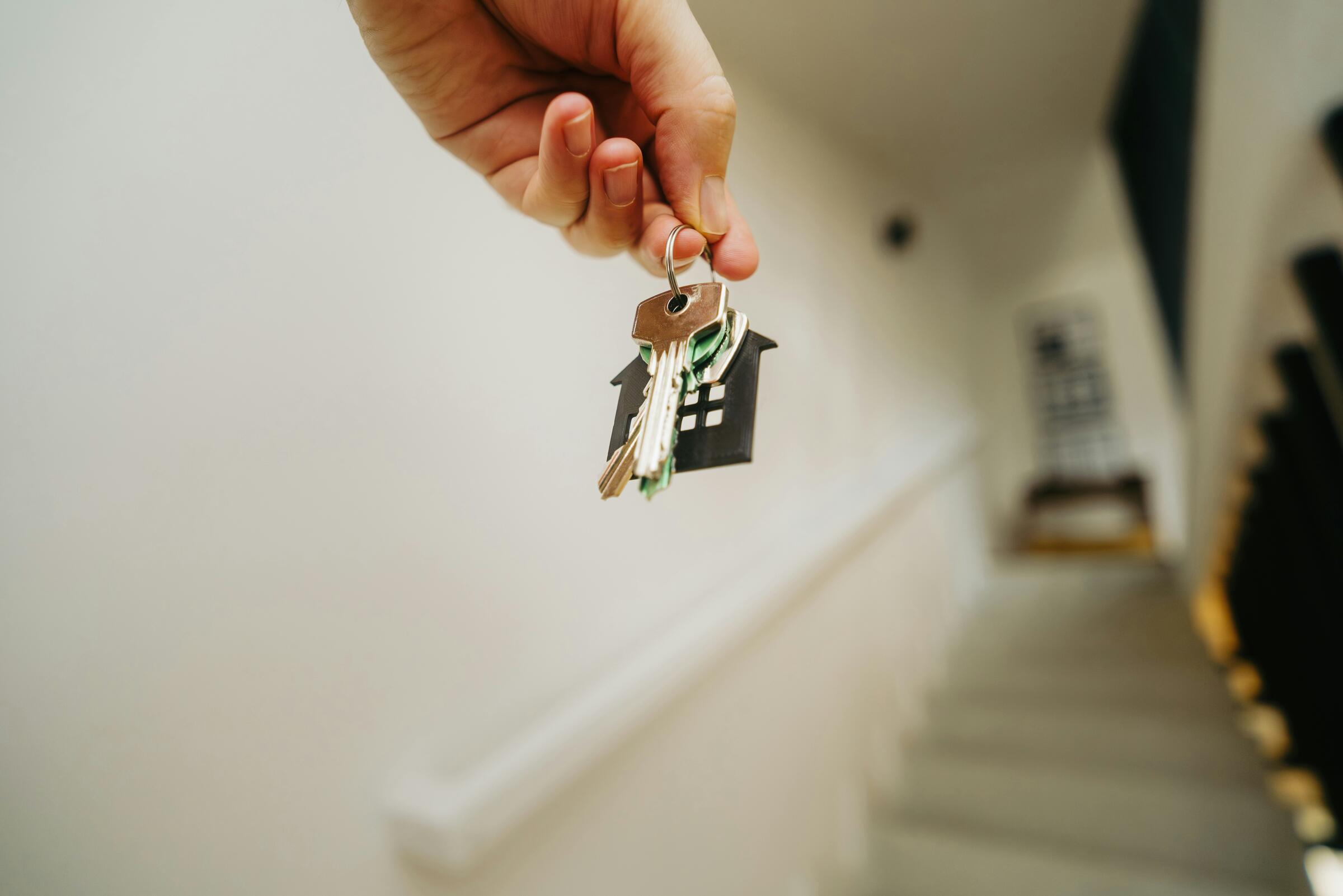 A hand holding house keys with a house-shaped keychain